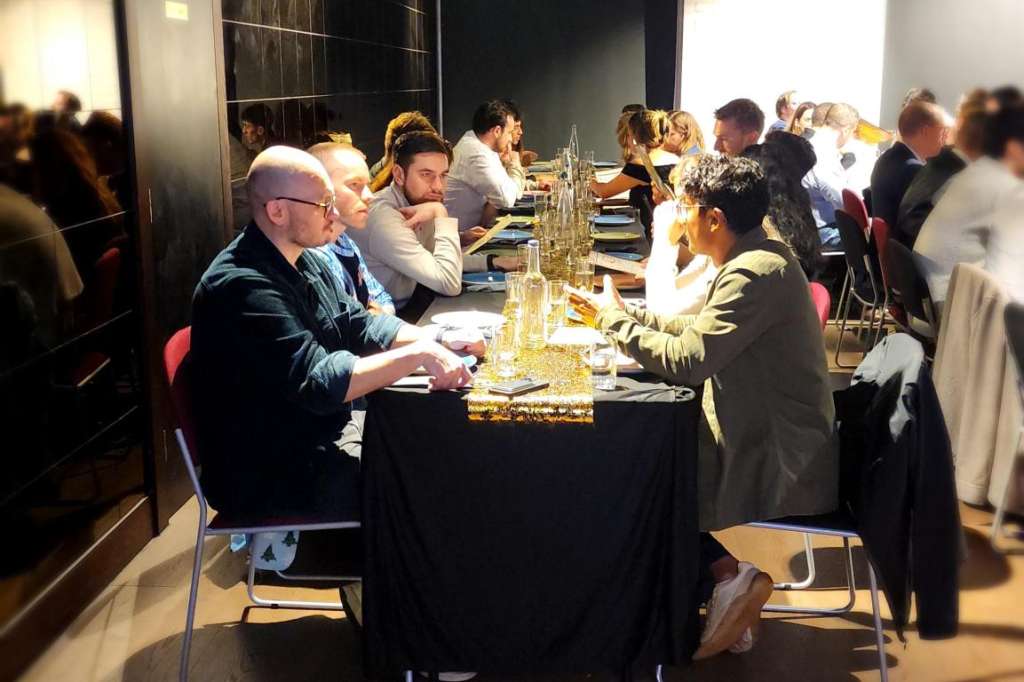 Modern event space with long black table set for seated dinner, multiple guests dining, industrial ceiling with spotlights.