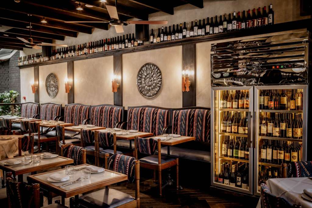 Fine dining restaurant interior with booth seating, place settings, wine display, and decorative wall features.
