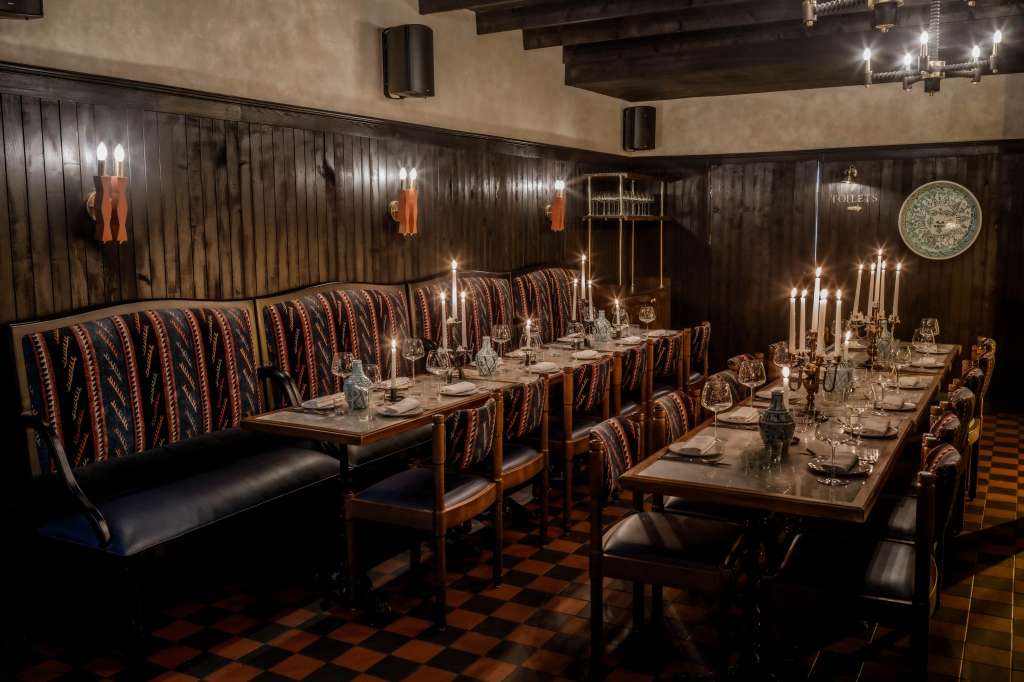 Main Restaurant set for a seated dinner with long tables, patterned banquette seating, candlelit centerpieces, and dark wood paneling.