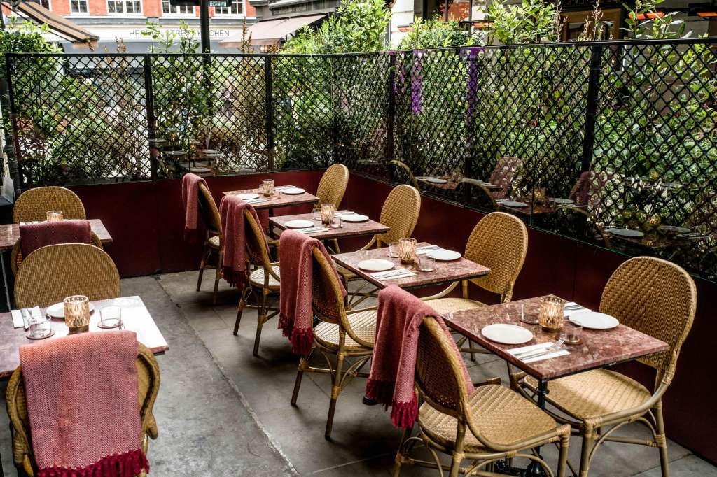 Outdoor terrace with multiple tables set for dining, wicker chairs, burgundy linens, and climbing ivy trellis.