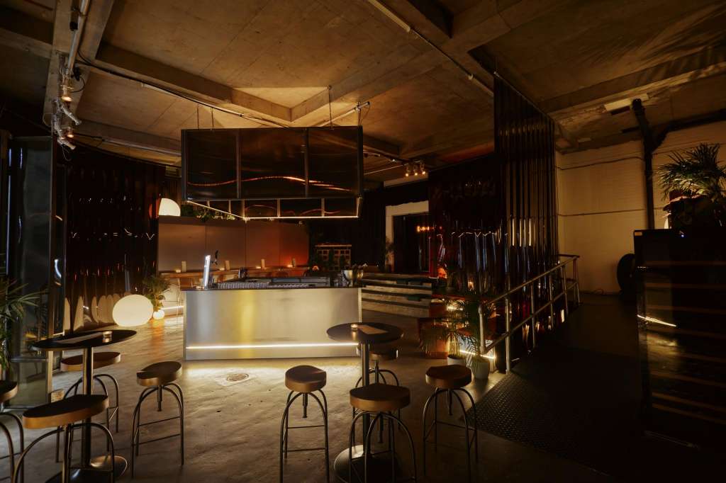 Modern bar and lounge space with illuminated counter, bar stools, and ambient lighting in an industrial venue.