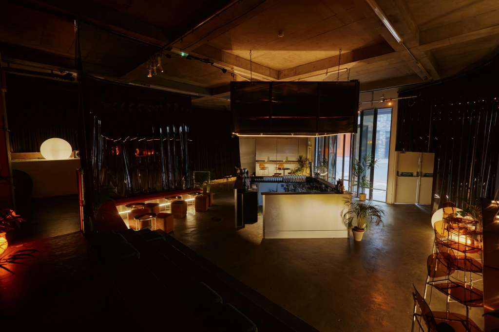 Modern event space with bar counter, ambient lighting, wooden ceiling, and open floor layout.