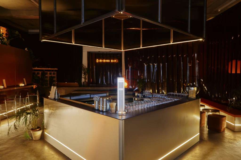Modern bar setup with illuminated counter, geometric black canopy, and ambient lighting in industrial space.
