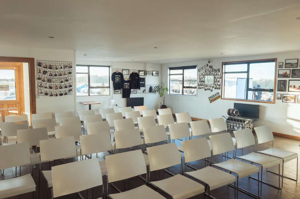 Briefing room with rows of cream chairs facing forward, large windows, and photo displays on walls.