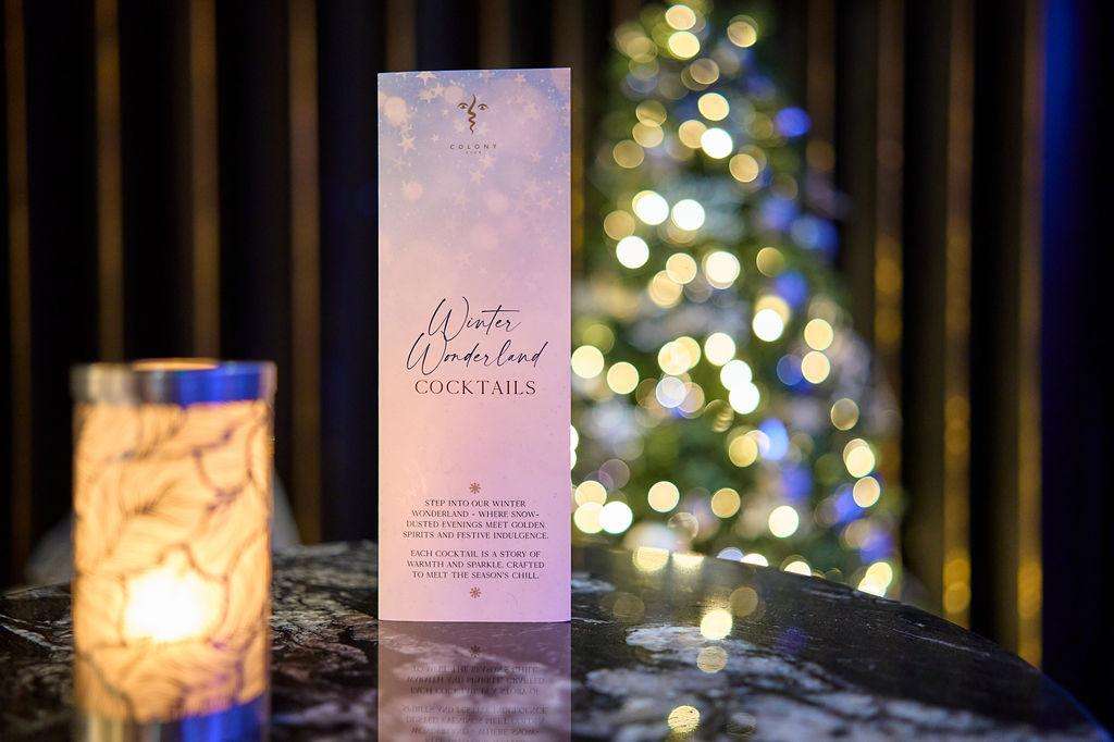 Lounge Bar styled for winter with cocktail menu card, lit candle, and decorated Christmas tree with warm and cool-toned lights.