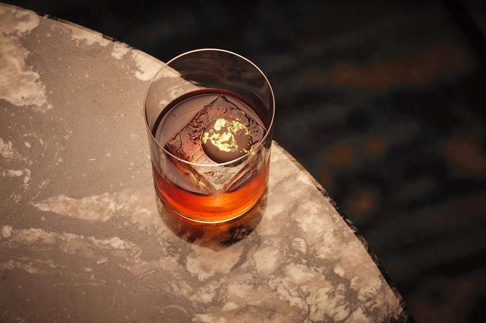 Whiskey glass with ice on marble surface, backlit by warm golden light.