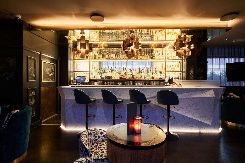 Lounge Bar with illuminated back bar, marble counter, black bar stools, and ambient lighting.