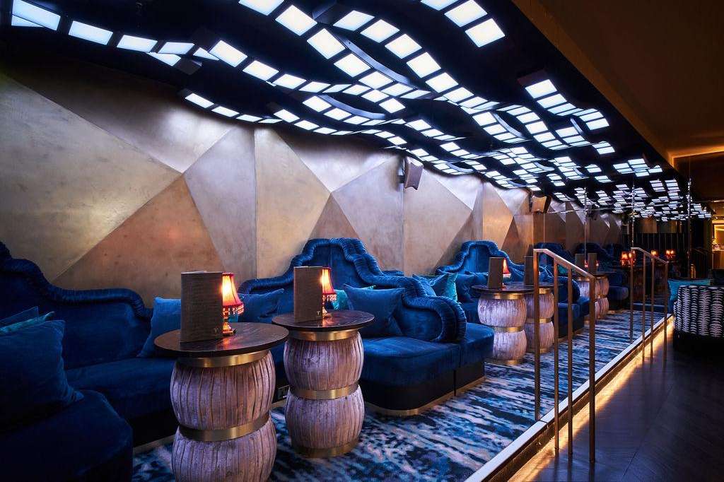 Lounge Bar with blue velvet seating, sculptural white ceiling elements, ambient lighting, and decorative side tables.
