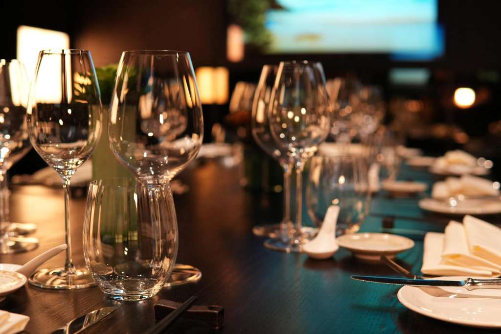 Formal dining table set with wine glasses, place settings, and ambient lighting along a long table.