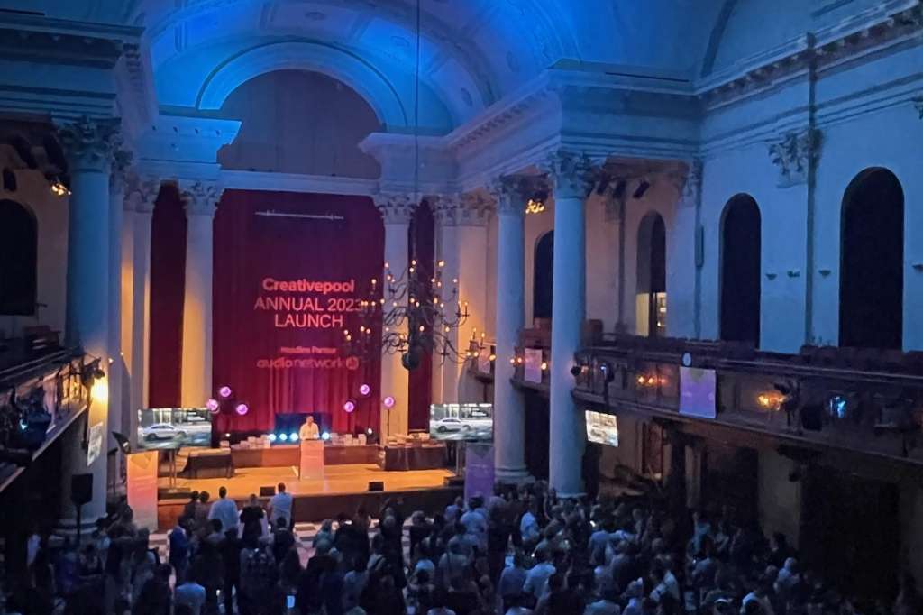 Grand hall with blue lighting, stage backdrop, and crowd gathered for a launch event.