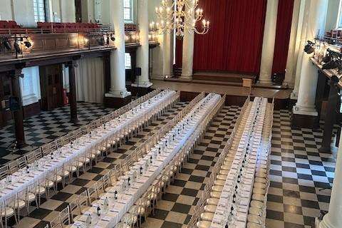 Grand hall with ornate columns and arched ceiling, set with long banquet tables and formal place settings.