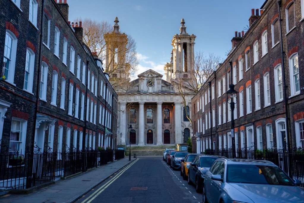 Exterior view of Smith Square Hall, a Georgian church building with columns and towers, framed by period townhouses on a clear day.