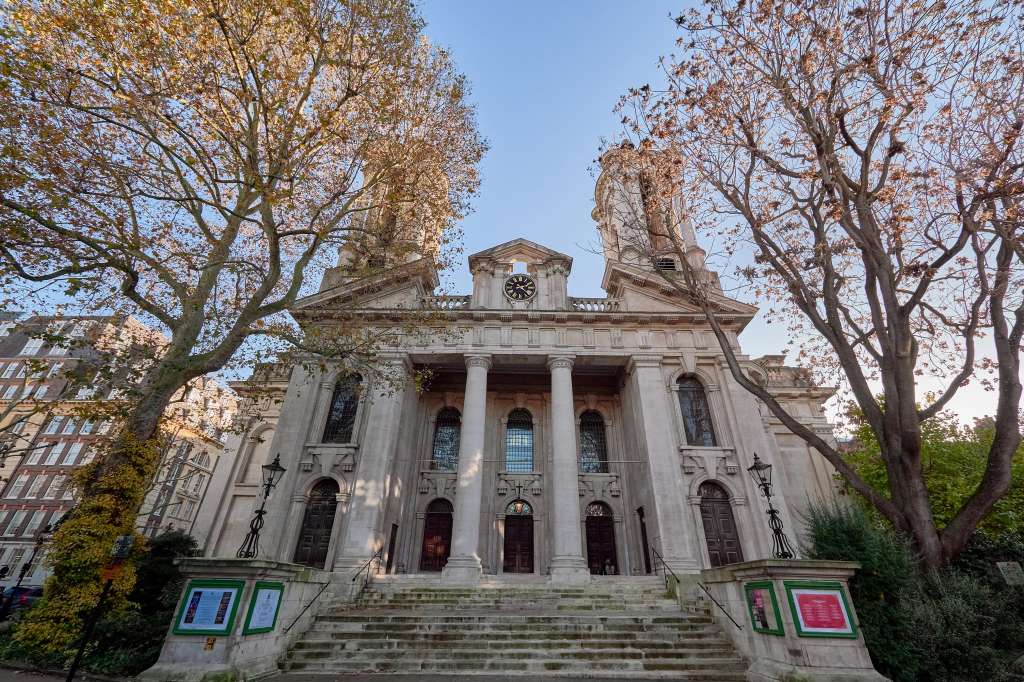 Neoclassical building exterior with columned facade, clock tower, and surrounding bare autumn trees.