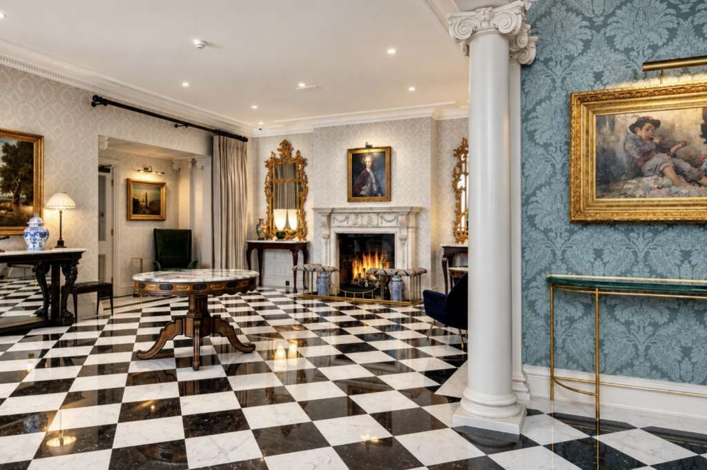 The Anne Machin Ballroom with black and white checkered marble floor, fireplace, ornate columns, and gilt-framed artwork.