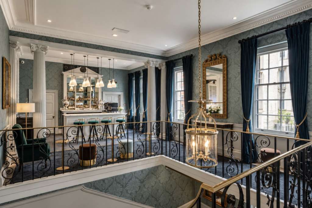 The Great Hall with a mezzanine bar featuring pendant lighting, ornate railings, and elegant furnishings overlooking the main space.