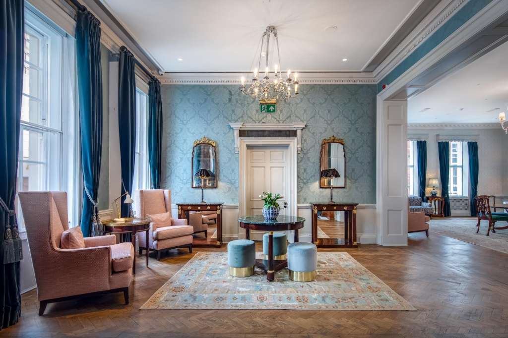 The Library with elegant seating arrangement, blue damask wallpaper, crystal chandelier, and period furniture.