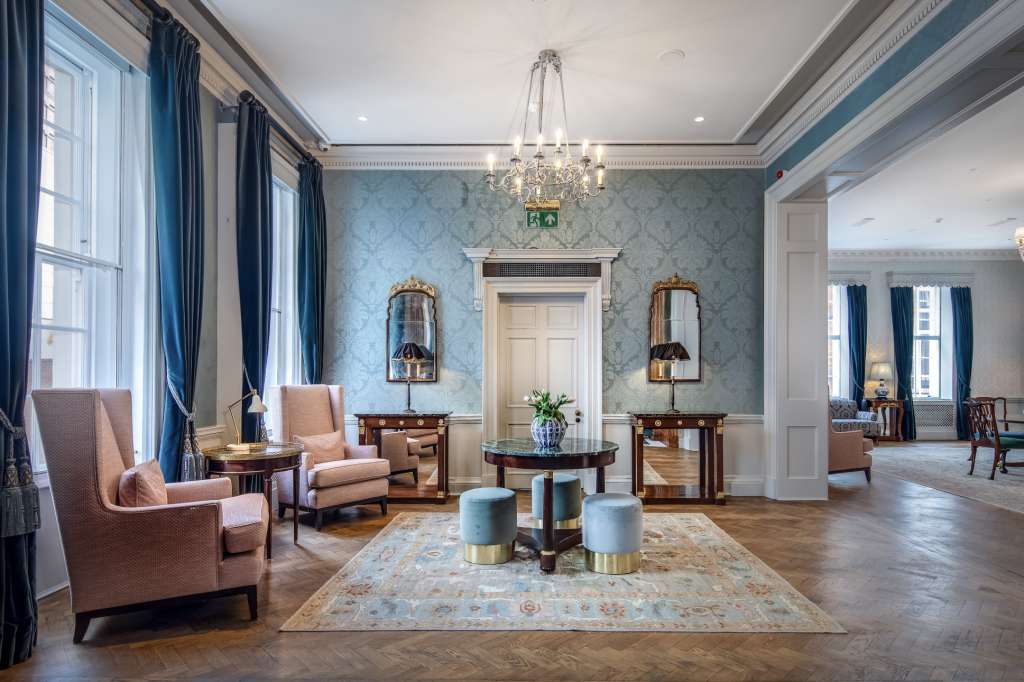 The Library with elegant seating arrangements, blue damask wallpaper, crystal chandelier, and hardwood flooring.