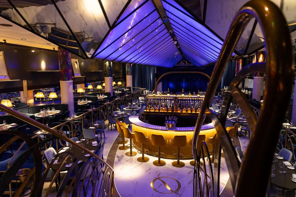 Upscale dining room with glass ceiling, purple ambient lighting, central bar, and round tables set for service.