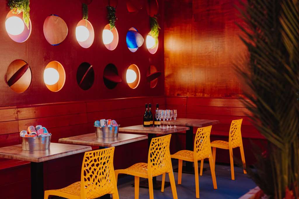 Bar area with red walls, illuminated circular decor, yellow chairs, and tables set with bottles and glasses.