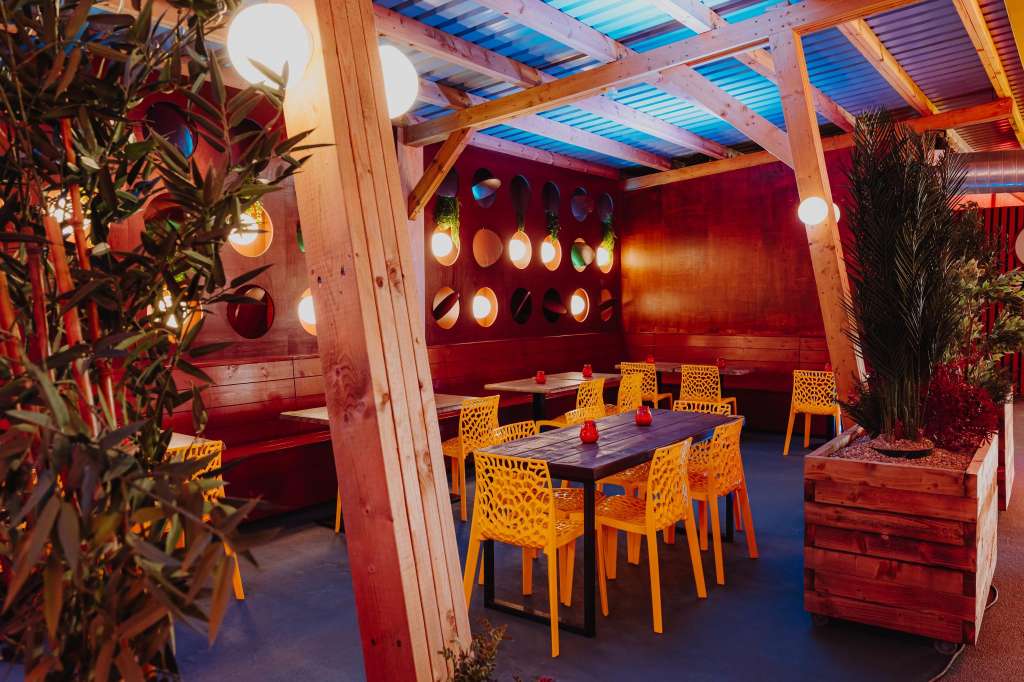 Yellow Zone set up with dining table, yellow chairs, red wall backdrop, wooden beams, and ambient lighting.
