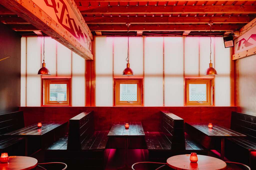 Hotel Milano Bar with red and black booth seating, copper pendant lights, and framed windows under industrial ceiling.