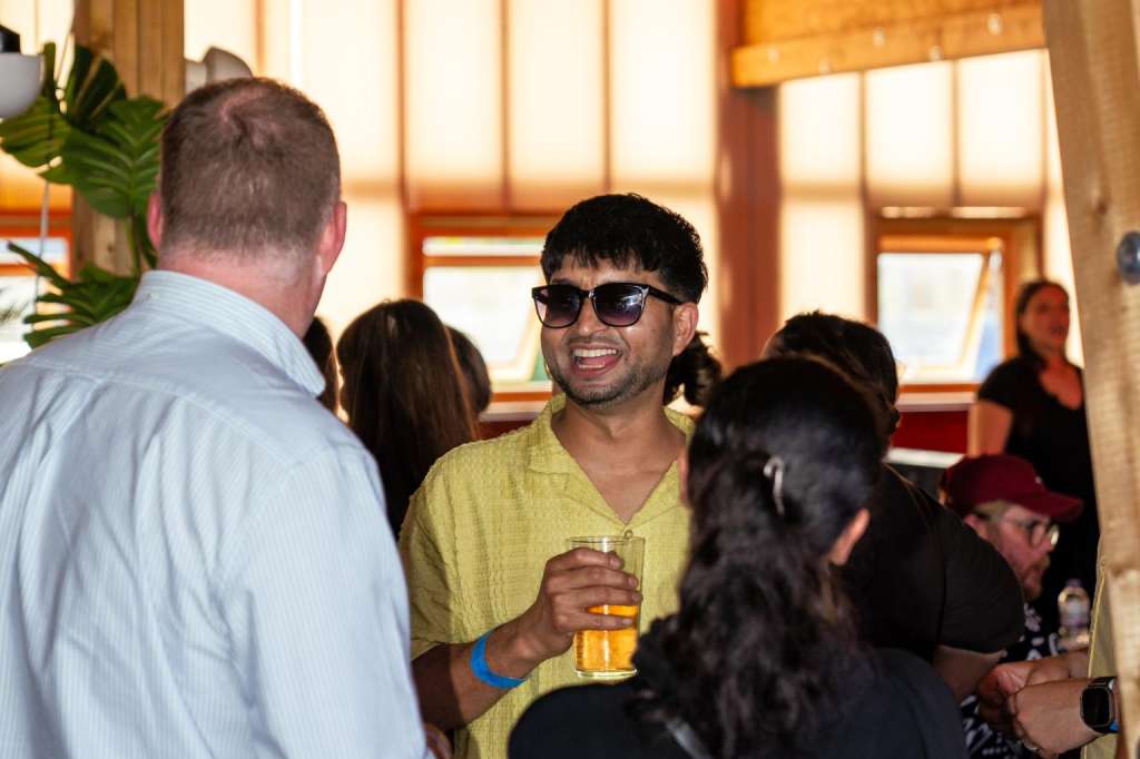 Hotel Milano Bar interior with guests mingling, holding drinks, warm wood beams and pendant lighting.