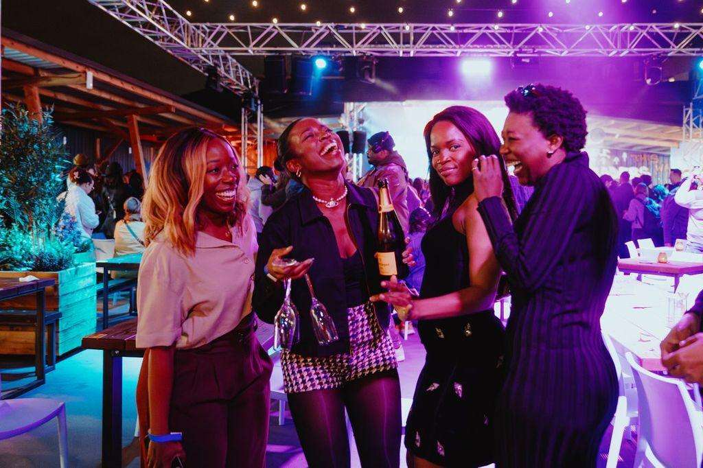 Large venue with purple and blue lighting, industrial truss, guests mingling with drinks and cocktail tables.