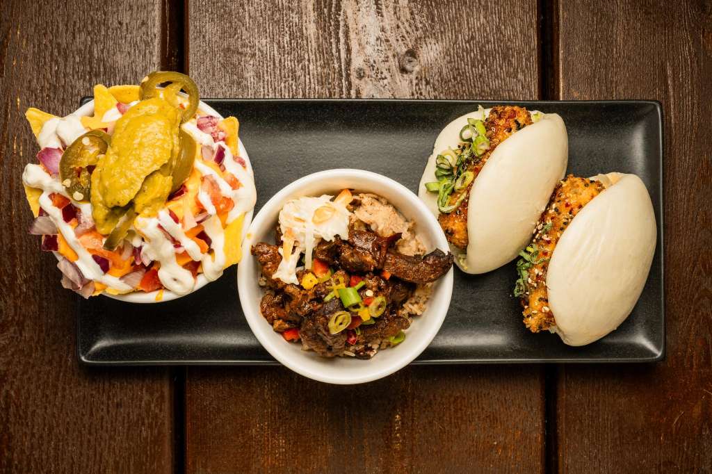 Close-up of plated food on dark slate: tacos, buns, and pickled vegetables on wooden surface.