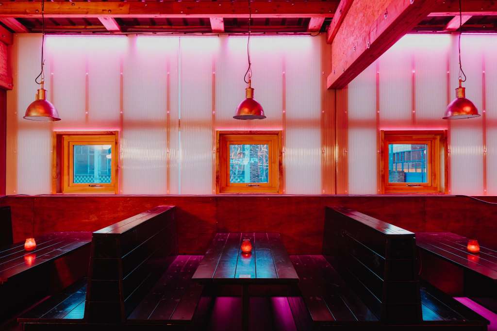 Hotel Milano Bar with red and pink ambient lighting, booth seating, pendant lamps, and industrial windows.