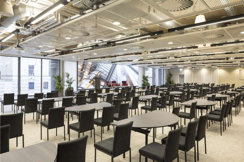 Modern open-plan space with round tables, black chairs, and floor-to-ceiling windows overlooking a city street.