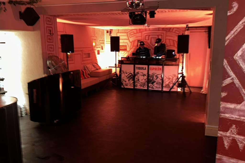 Event space with DJ booth, red ambient lighting, geometric wall patterns, and lounge seating.