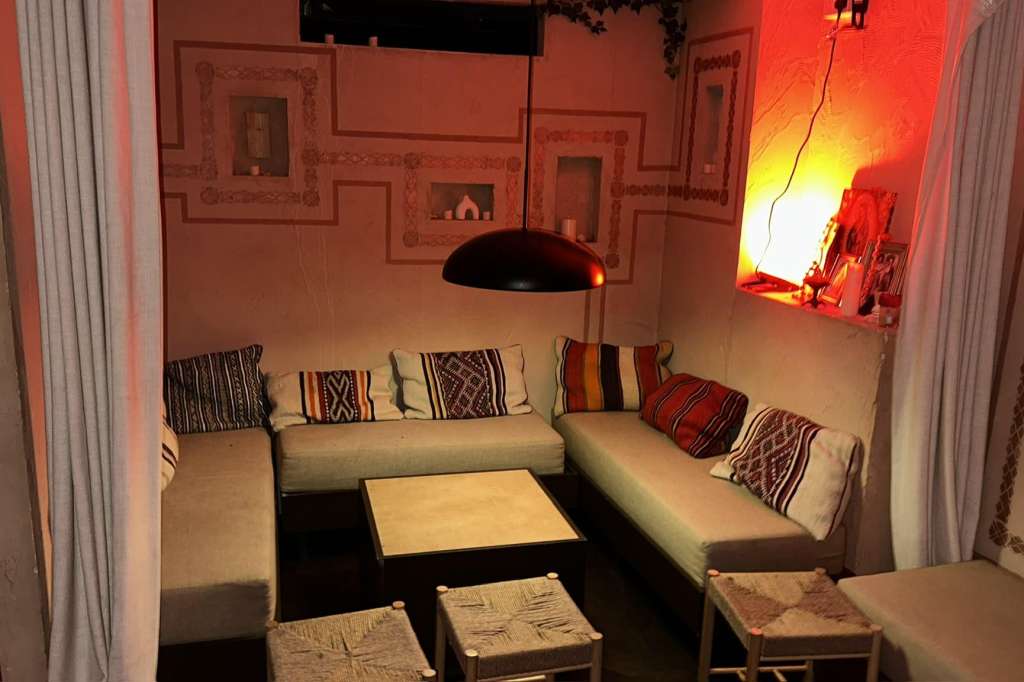 Lounge area with L-shaped seating, patterned cushions, pendant lighting, and warm ambient red-orange lighting.