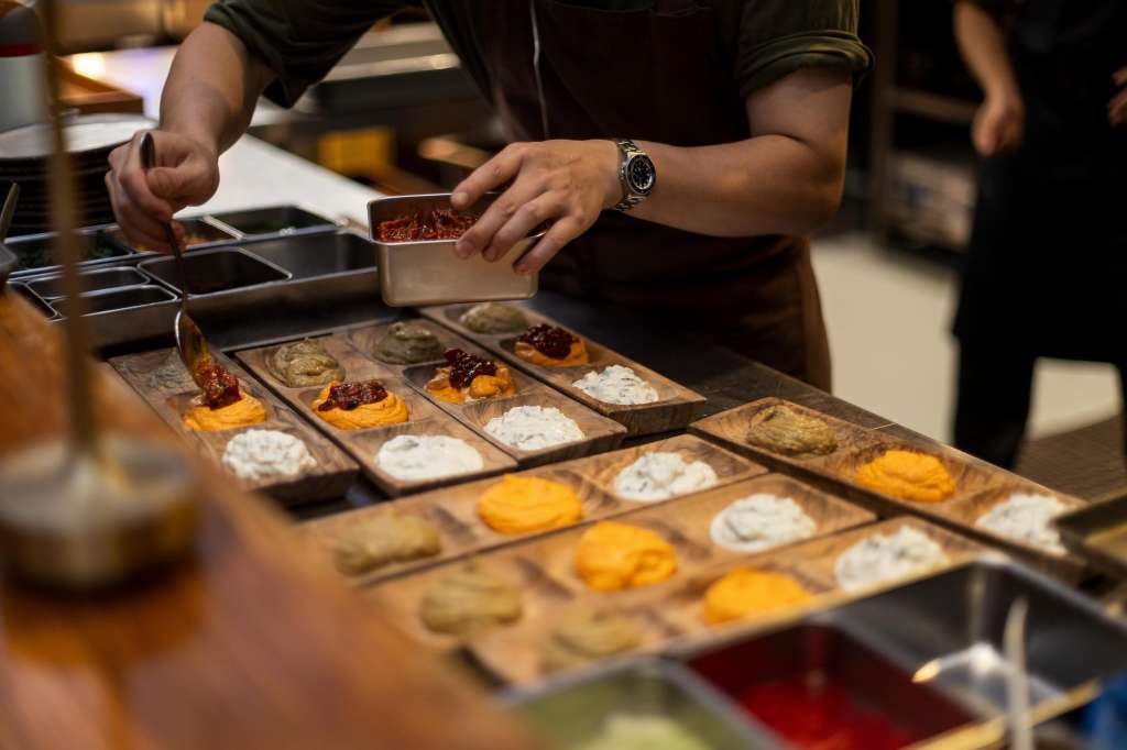 Chef plating appetizers with garnish on a service counter during food preparation.