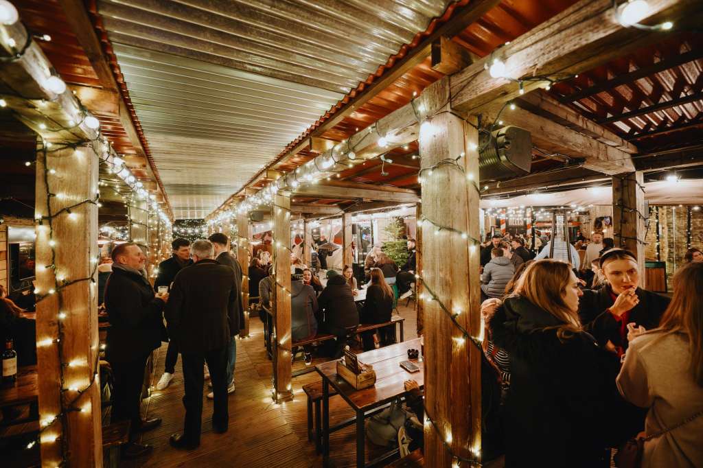 Outdoor terrace with wooden pergola, string lights, and wooden columns. Guests mingling in evening attire.