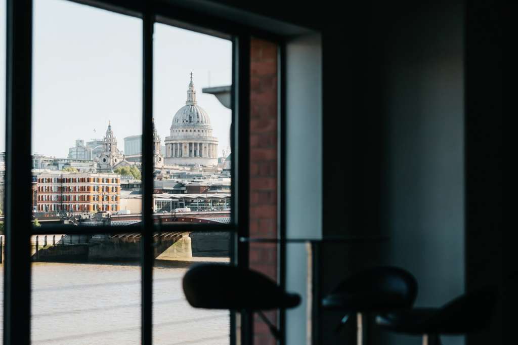 Interior view through large windows overlooking St. Paul's Cathedral and Thames riverfront with modern seating in foreground.