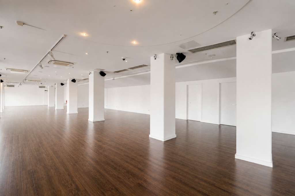 Open gallery space with white columns, wooden flooring, recessed lighting, and white wall panels.