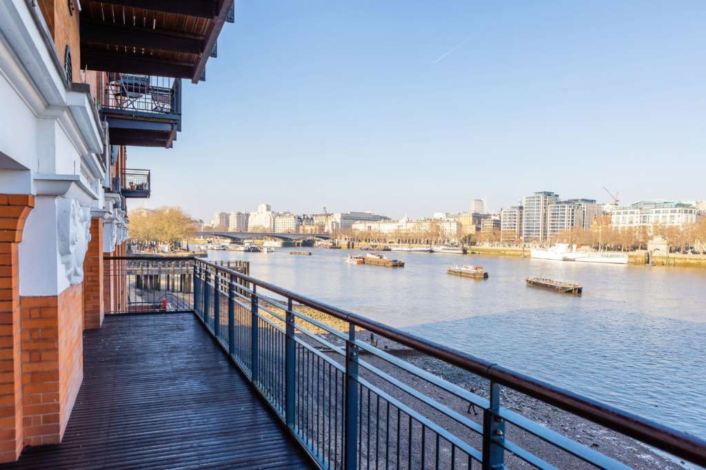 Riverside terrace with metal railings overlooking the Thames, bare trees, and city skyline.