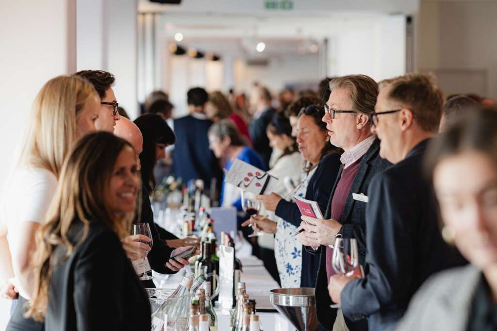 Guests mingling at a standing reception with wine glasses and catering table, modern interior with pendant lighting.