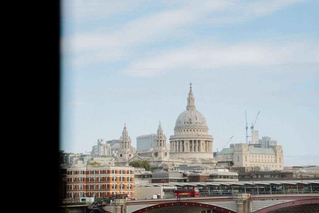 London skyline view with St. Paul's Cathedral, Thames river, red tour boat, and Millennium Bridge.