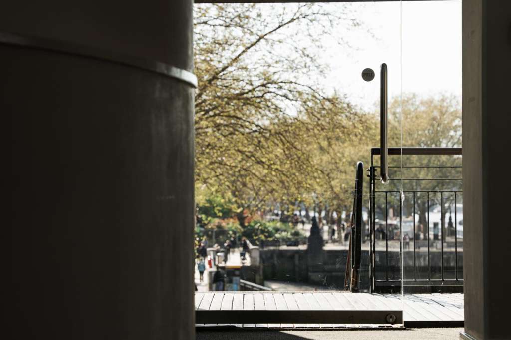 Interior corridor opening onto an outdoor terrace with spring foliage and crowds visible in the distance.