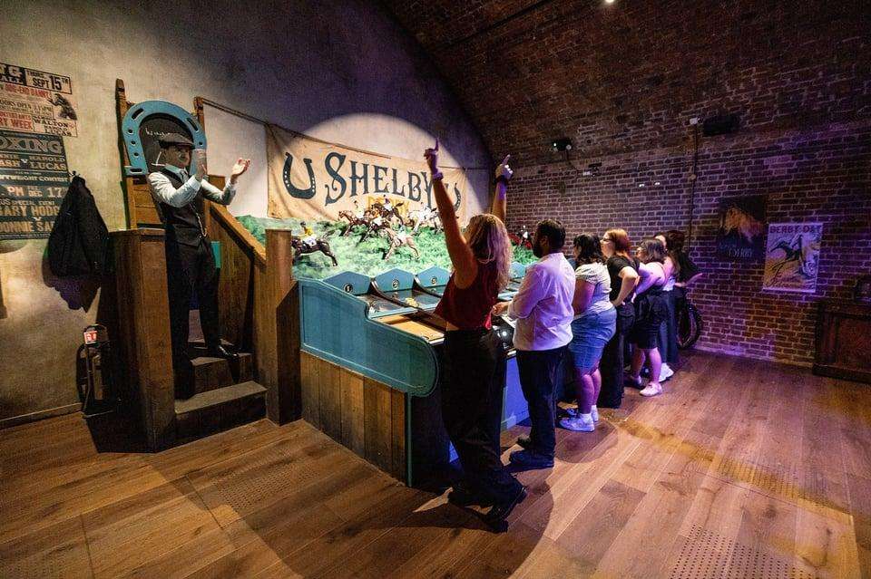 Interior bar area with period decor, wooden counter, and group of visitors standing and observing displays.