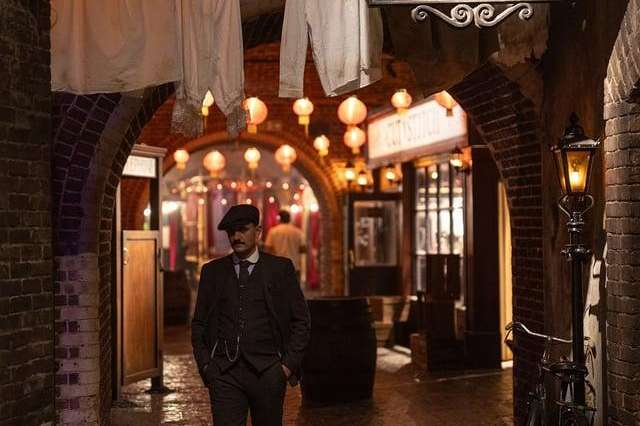 Atmospheric alleyway with brick walls, vintage signage, warm lantern lighting, and period costume figure.
