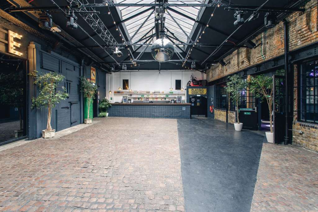 Industrial warehouse space with exposed brick, steel roof structure, bar counter, and open floor plan.