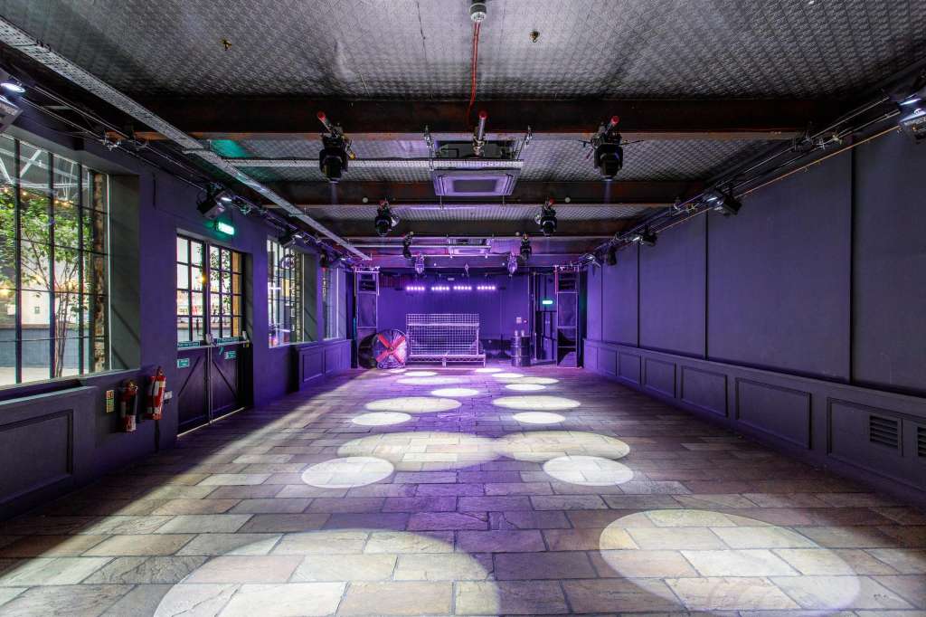 Industrial event space with purple ambient lighting, stage setup, and professional rigging overhead.
