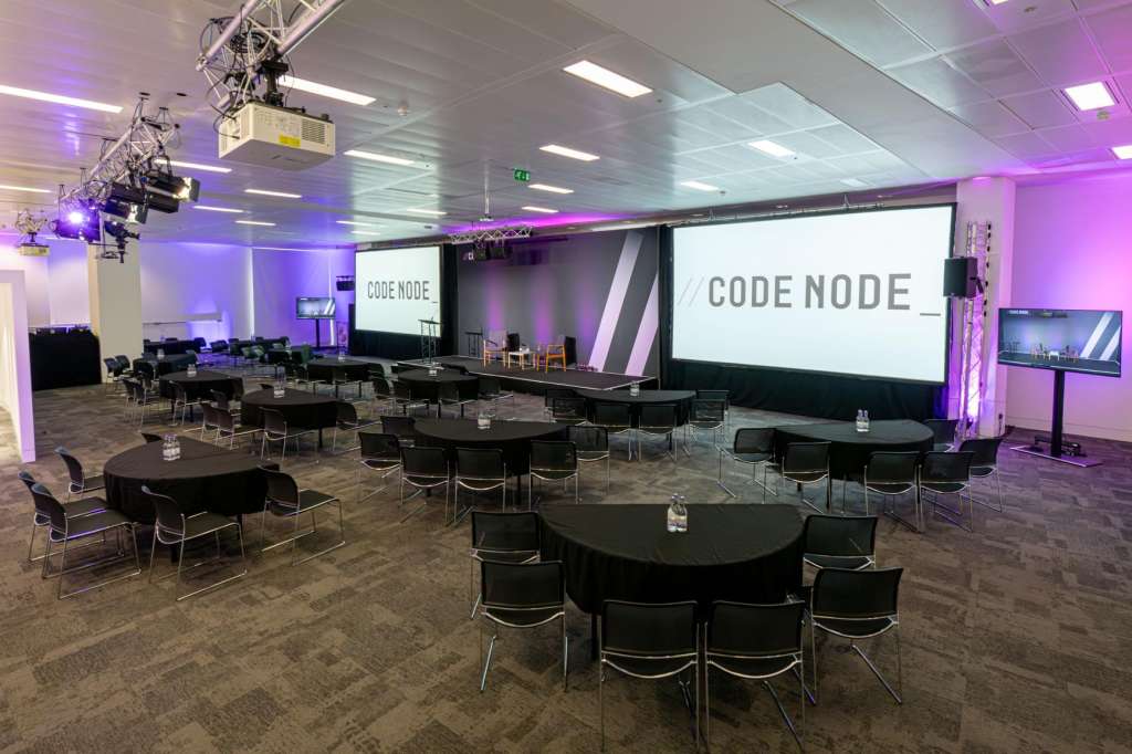 Large event space with round tables, chairs, projection screens, and purple ambient lighting throughout.