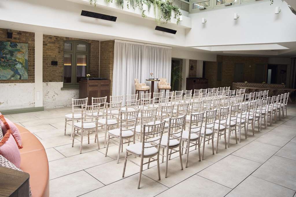 Chelsea Rooms set with rows of white Chiavari chairs facing a small stage, brick walls, and draped curtains.