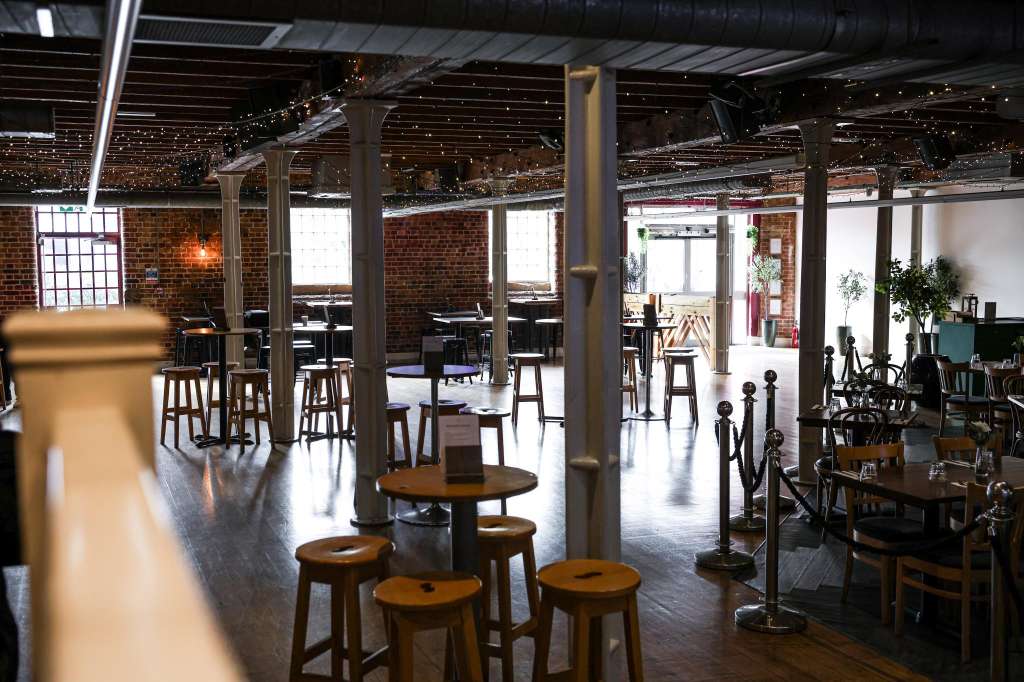 Warehouse Bar with exposed brick, string lights, high tables, bar seating, and industrial columns.