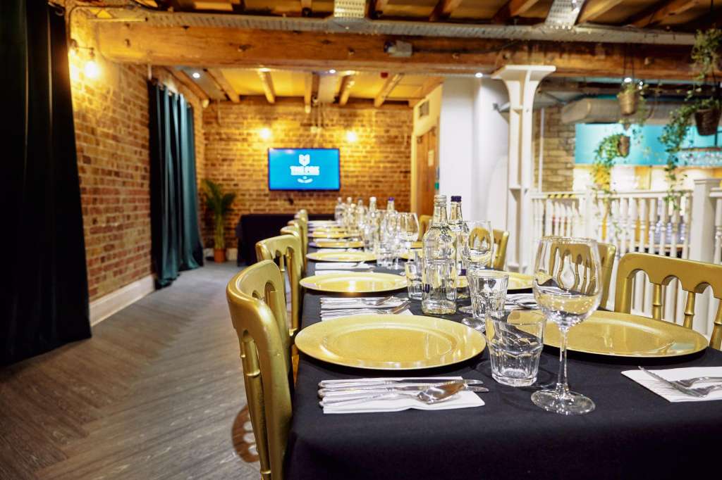 Warehouse Bar set for a seated dinner with long table, gold chairs, place settings, glassware, and exposed brick walls.