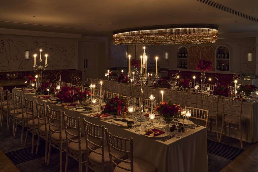Dining Room set for a formal dinner with long tables, burgundy floral centerpieces, candlelit candelabras, and crystal glassware.