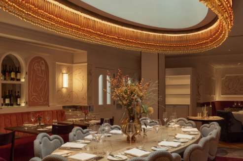 Dining room with oval table set for formal dinner, upholstered chairs, dramatic gold oval chandelier, and ambient lighting.